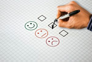 hand checking boxes with smiley face, neutral face, and sad face