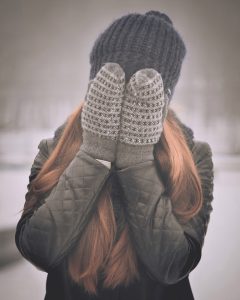 person covering their face with mitten-covered hands